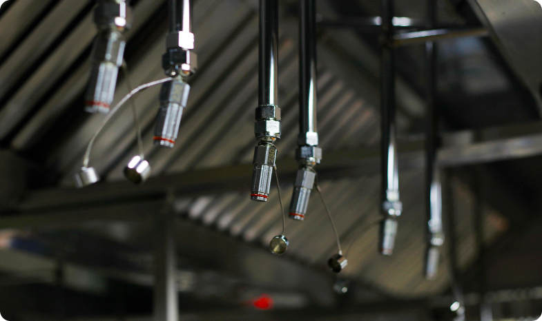 Pipes of a kitchen fire suppression system hang from the ceiling of a kitchen in a catering business